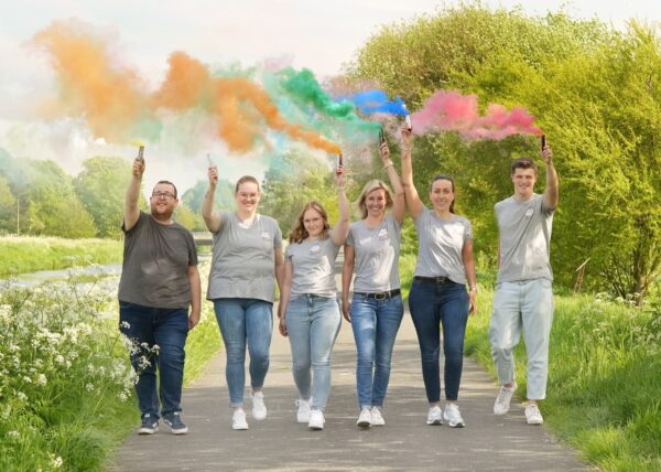 Teamfoto der Kita Arche Mittegroßefehn in dem die Erzieher*innen bunte Rauchfackeln hochhalten 