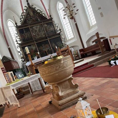 Blick in die Kirche Victorbur, zu sehen ist der Altar, das Taufbecken und davor liegen auf einer kleinen Decke auf dem Boden eine kleine Gitarre, eine Kerzenlaterne, eine Klangschale und ein beschriftetes und bemaltes Kreuz.
